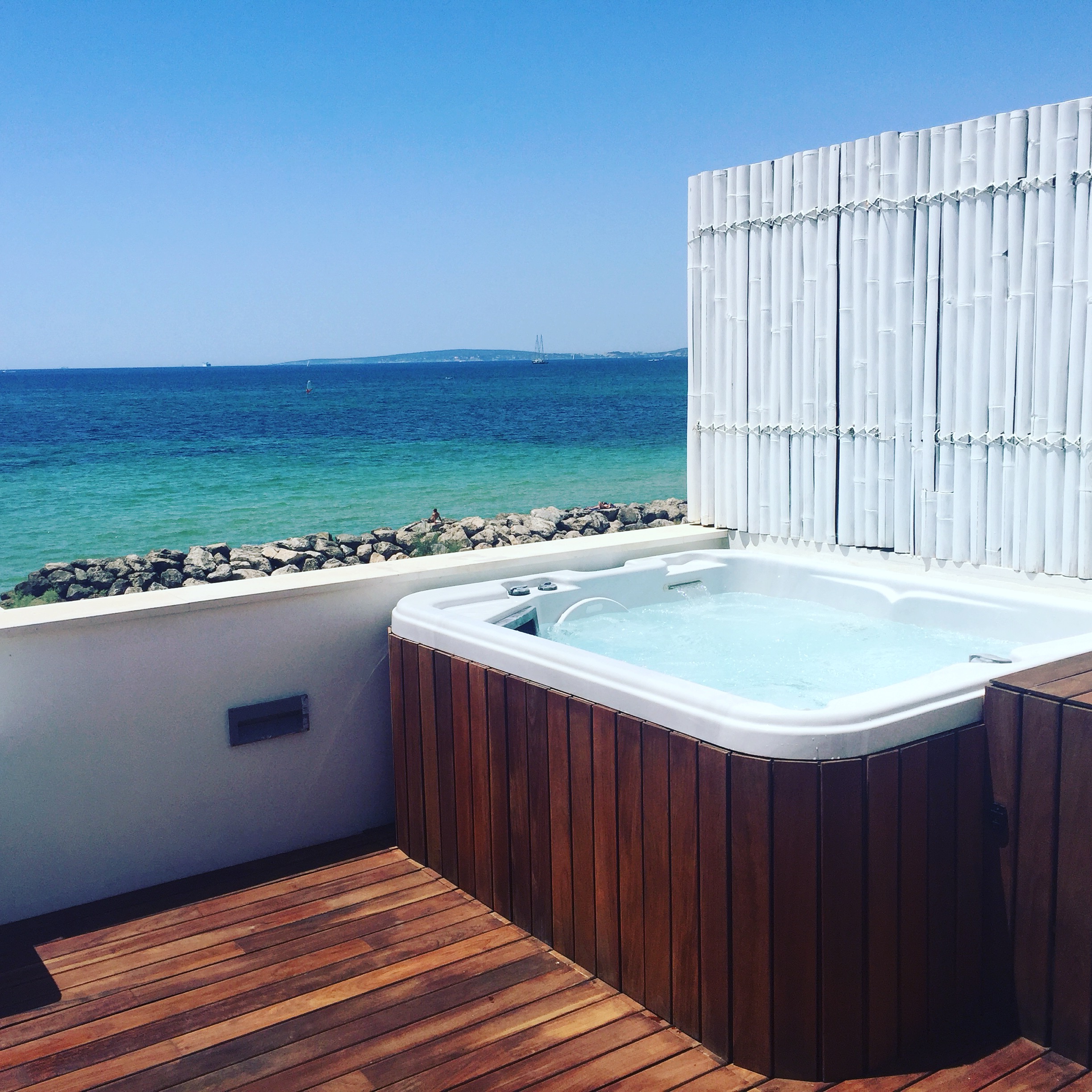 Coastal hot tub installation with white bamboo privacy fence and sea view