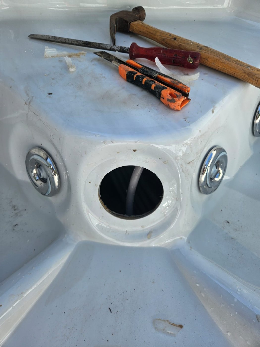 The light opening in the spa shell after the lamp unit was taken out, with the supply cable visible and the tools laid on the moulded surround