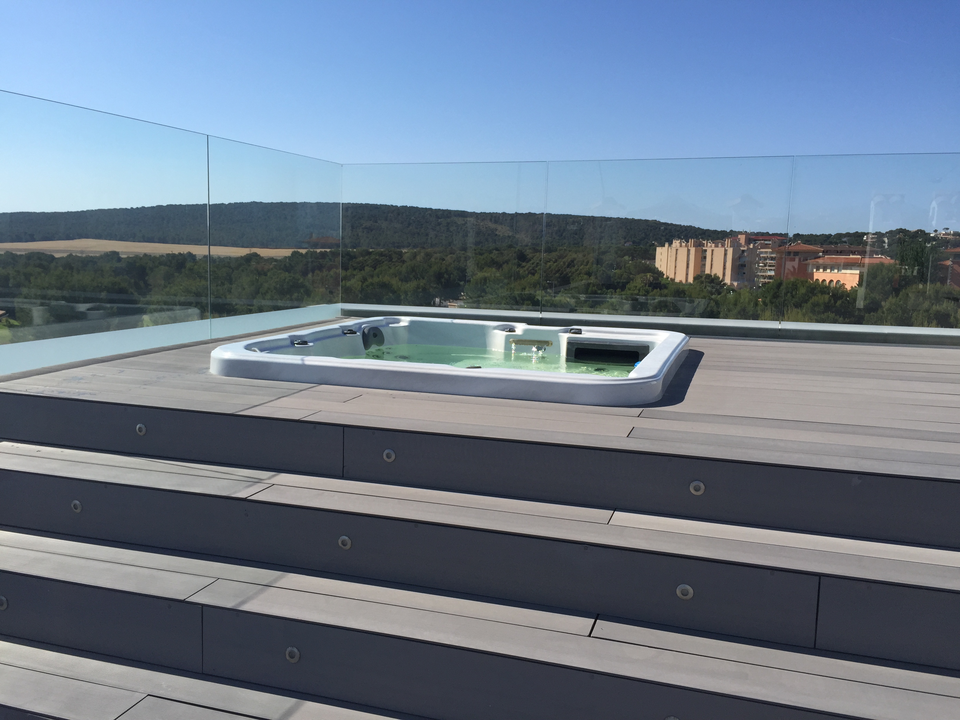 Modern whirlpool on a grey deck with glass railing overlooking the Mallorca landscape