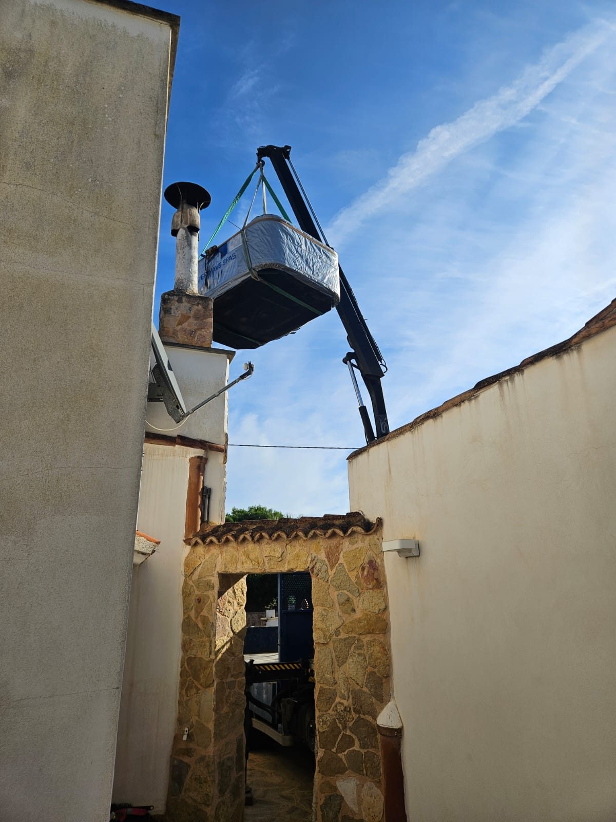 Crane lifting the whirlpool high between the houses into the courtyard in Cala Santany&iacute;